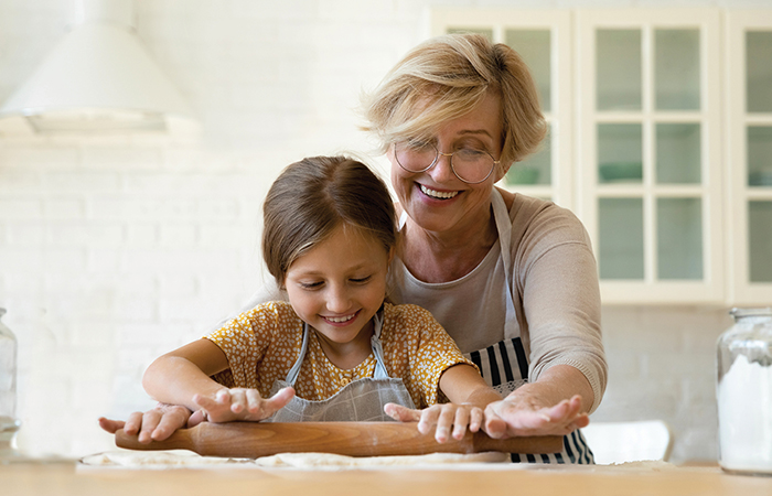 Grandma helping young girl roll out dough