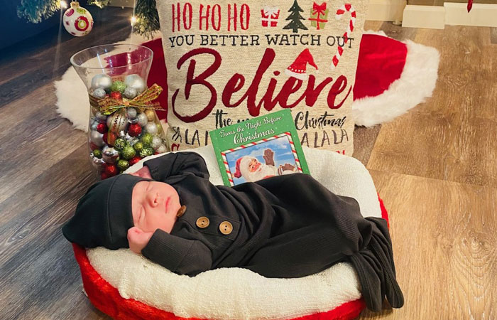 Baby Blake laying in a Christmas baby bed in front of a Christmas tree.