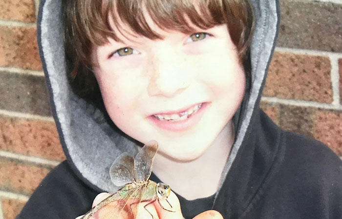 Bryce holding a flying insect while smiling at the camera