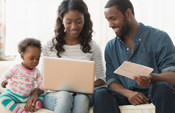 Young black couple and baby sitting on couch looking at finances on a laptop