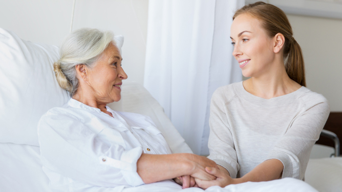 Senior woman in hospital bed with young woman holding her hand