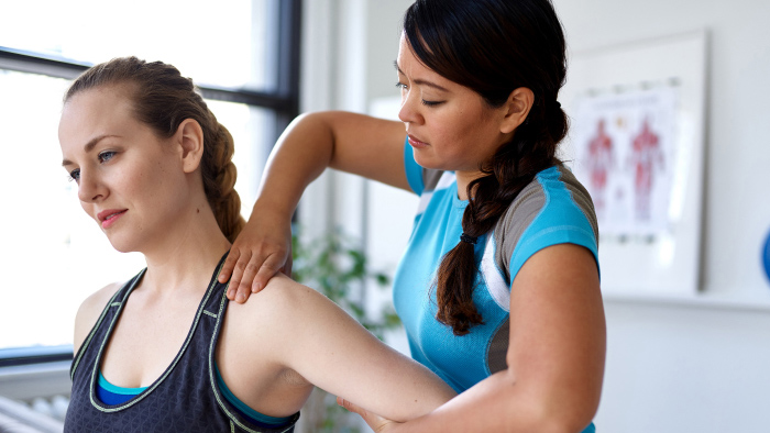 Female physical therapist working shoulder of female patient