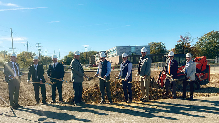 Hospital officials in construction helmets and hold shovels at groundbreaking ceremony