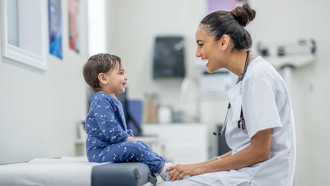 Toddler sitting on clinic cot smiling at female nurse