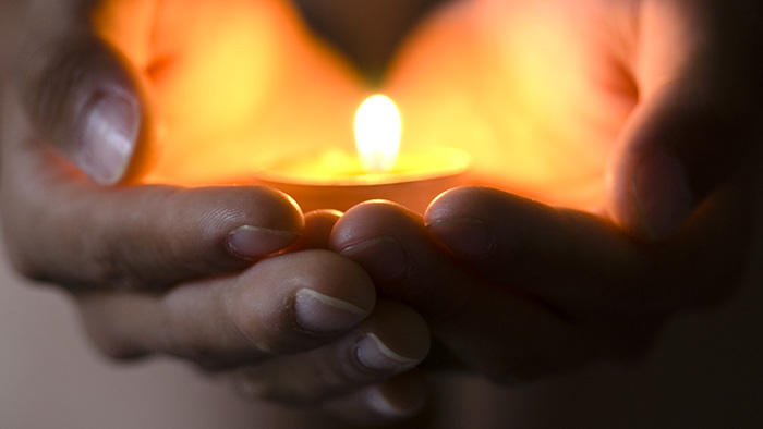 Hands holding a lighted votive candle