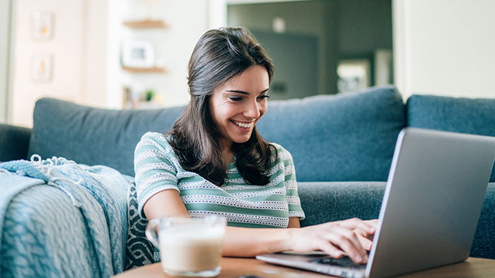 Young woman sitting in front of blue couch with laptop